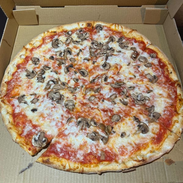 A whole mushroom pizza with one slice removed, sitting in a cardboard delivery box.
