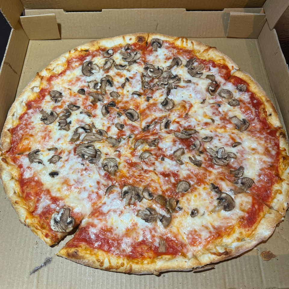 A whole mushroom pizza with one slice removed, sitting in a cardboard delivery box.