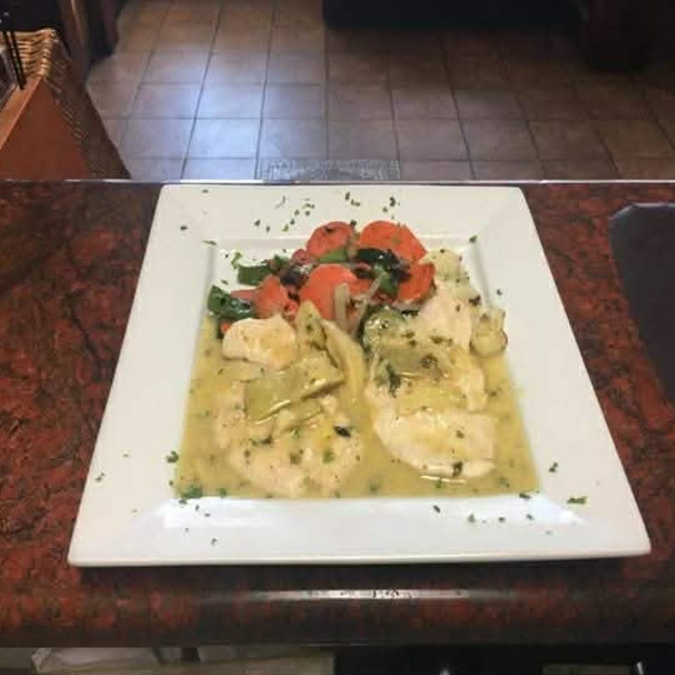 Chicken in a creamy sauce with roasted red peppers and green vegetables on a white plate.