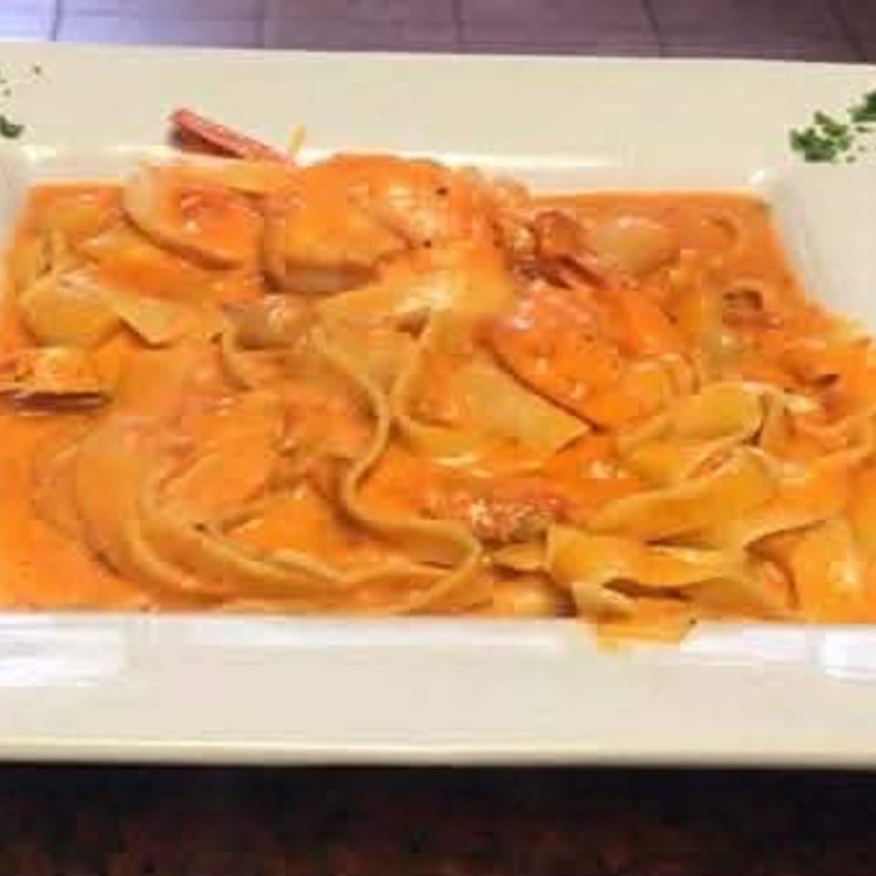 Fettuccine pasta in a creamy orange sauce with shrimp and parsley garnish on a white plate.