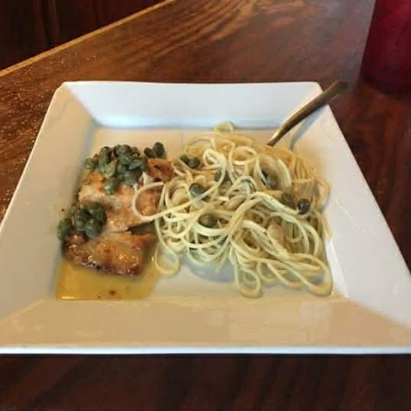 Chicken piccata with capers and spaghetti on a white rectangular plate.