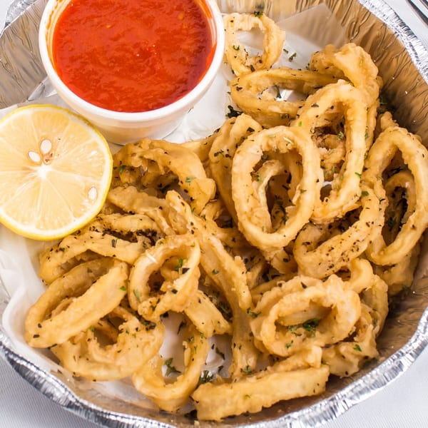 Fried calamari rings with a side of red marinara sauce and a lemon wedge in a foil container.